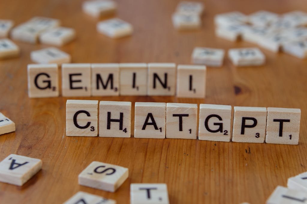 Close-up of wooden Scrabble tiles spelling Gemini and ChatGPT on a wooden surface.
